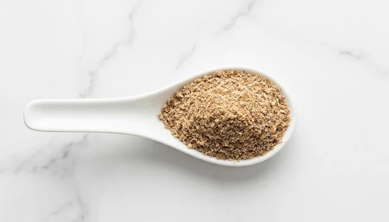 One ounce of ground flaxseed meal measured in a white ceramic spoon on a marble counter
