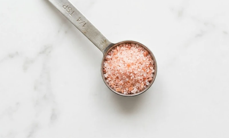 Fine pink Himalayan salt measured in a quarter teaspoon spoon on a white marble counter